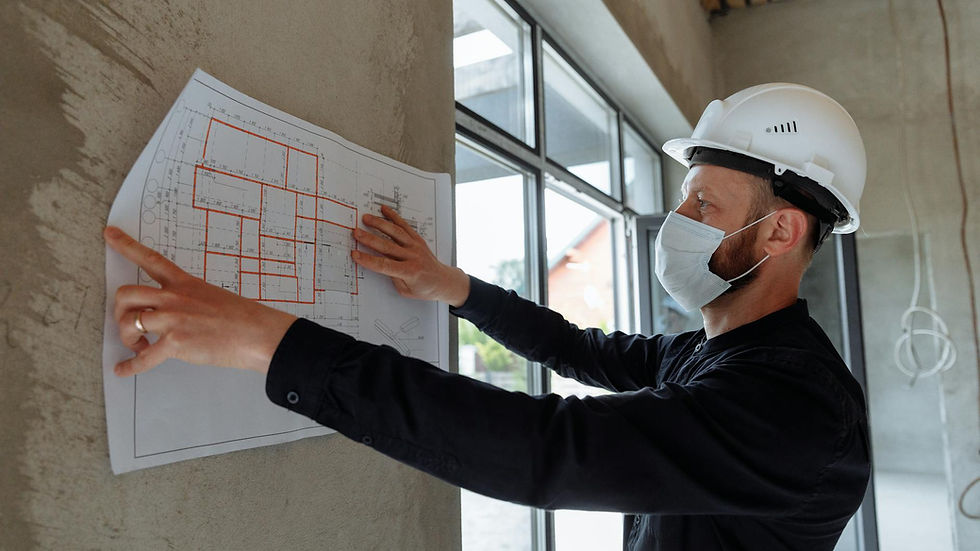 Architect wearing hard hat and mask reviews floor plans on site for new construction project.