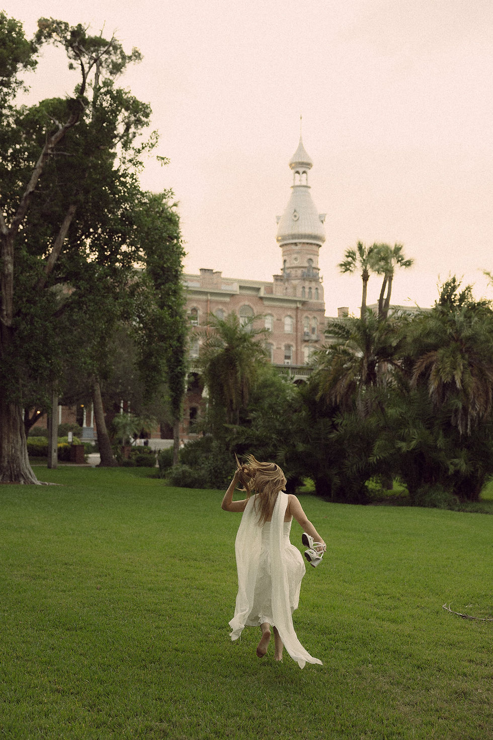Woman in white dress running on lawn toward historic tower