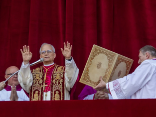 Clergy in ornate robes stand before a red curtain. One man raises hands in blessing, flanked by assistants holding an elaborate book.