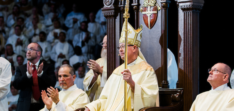 A bishop sits on the cathedra, holding his crozier, during the liturgy.