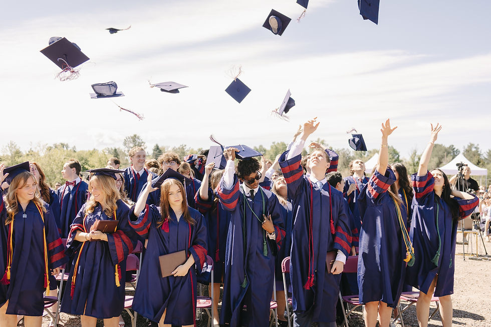 Graduates in blue gowns toss caps at an outdoor ceremony, smiling under a bright sky.