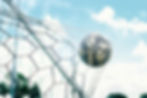 Soccer ball caught in a white net on a goal frame against a bright blue sky with clouds.