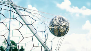 Soccer ball caught in a white net on a goal frame against a bright blue sky with clouds.