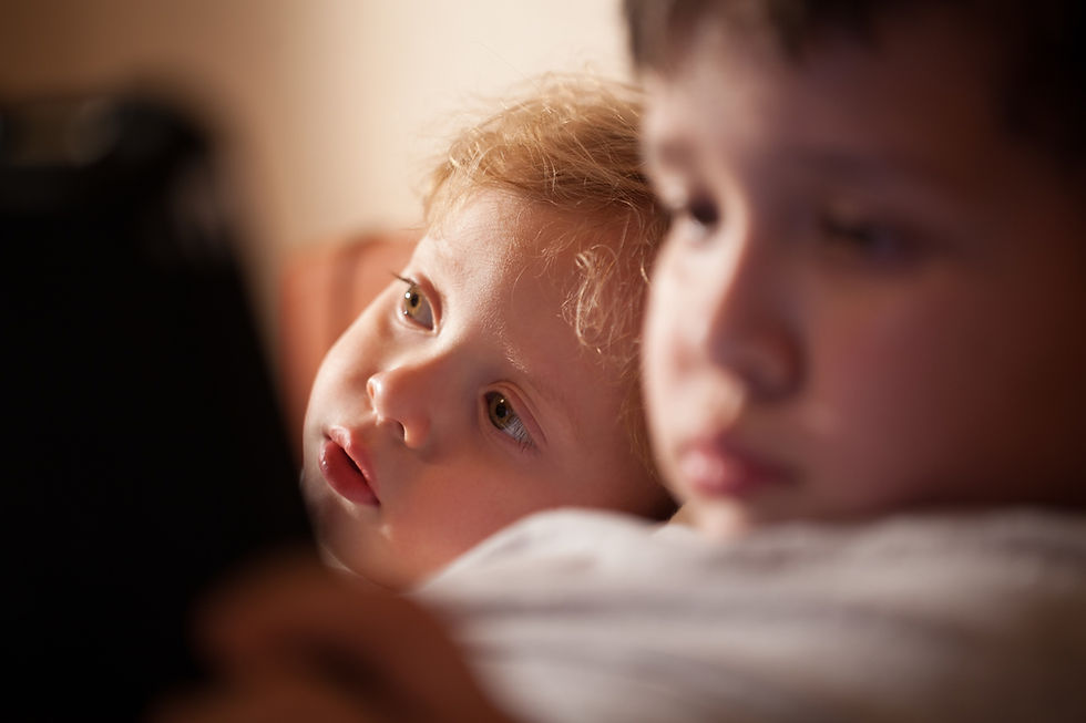 Two young children in warm indoor light, one blond child gazing upward while the other sits blurred in the foreground.