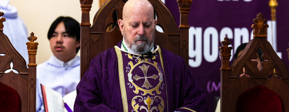 Bishop in ornate purple vestments sits solemnly on a wooden chair. "Believe in the gospel" text on a purple banner in the background.