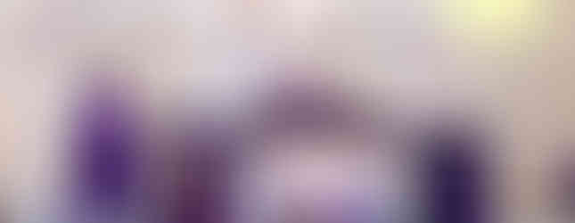 Bishops in purple robes celebrate Mass at an ornate church altar with a crucifix. One holds a chalice. Candles and text on screen visible.