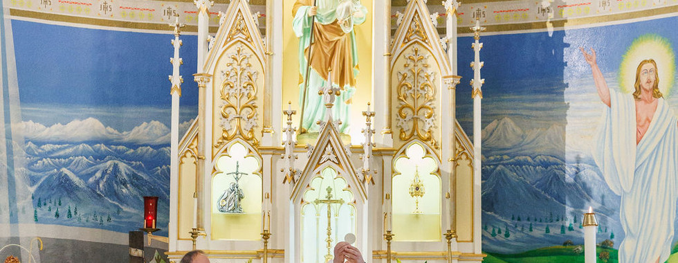 A priest elevates the Eucharist during Mass beneath a decorated altar and painted church apse.