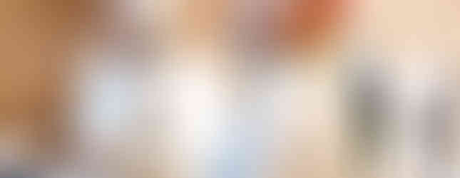 A clergy member and a woman in white look upward in a sunlit brick hall. Others are visible in the background, creating a focused atmosphere.