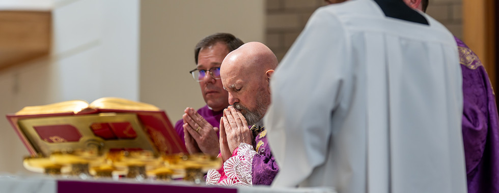 Bishop and clergy in purple robes pray at an altar with an open book and chalices. Sacred and reverent atmosphere.