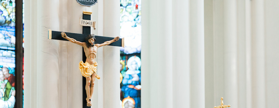 Crucifix labeled "Jubilee Cross" in a church with stained glass backdrop. A golden altar ornament with a cross is visible nearby.