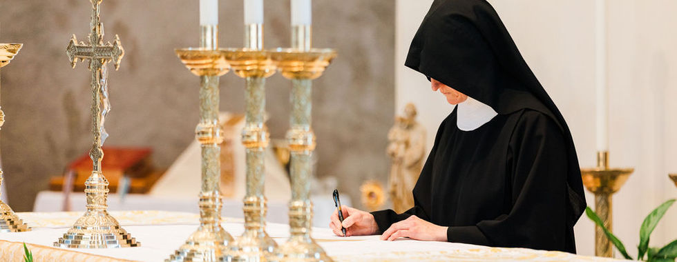 A sister signs her vows on the altar during the liturgy, surrounded by candles and sacred vessels.
