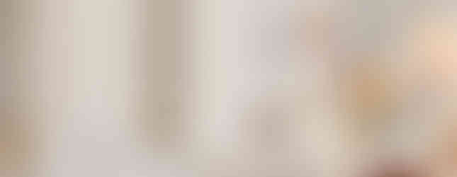 Bishop in ornate white and gold robes speaks at a lectern in an ornate church setting with carvings and religious figures in the background.