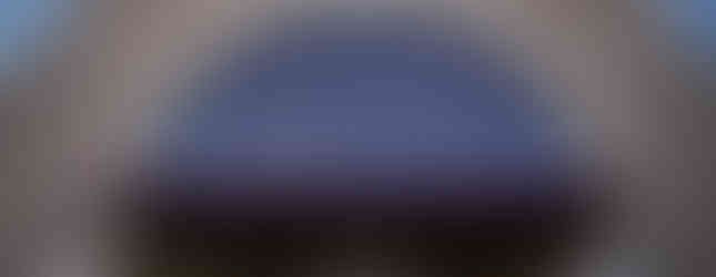 People gather outside a stone church, with three clergy in white heading towards an altar, under a clear blue sky.