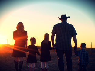 A family of five, holding hands, stands in silhouette against a vibrant sunset. They are in open country, with a peaceful, warm ambiance.