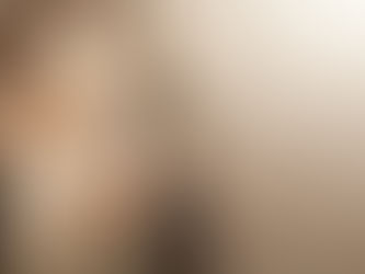 A person in a brown shawl and textured white dress cradles their pregnant belly. Soft warm lighting creates a peaceful mood.