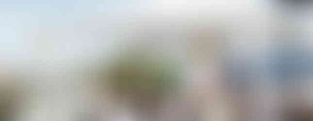 A bishop in ceremonial attire speaks to seated clergy under a tent in an outdoor religious event. The mood is solemn and formal.