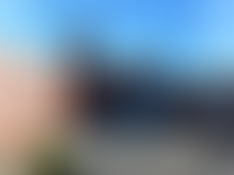 Brick building with large windows and bell tower against blue sky. Fenced playground in front. Calm and sunny atmosphere.