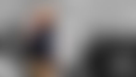 Hombre sonriente saluda mientras gente aplaude en fondo. Color sobre él y mujer, resto en blanco y negro. Ambiente de celebración.