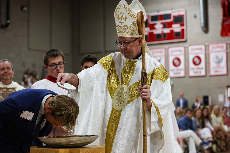 A bishop in ornate robes baptizes a person in a church setting, pouring water over their head. Red banners hang in the background.