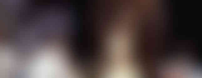 Clergymen in white robes at a ceremony. One sits on an ornate chair, wearing a mitre. Dark background, solemn mood, religious setting.