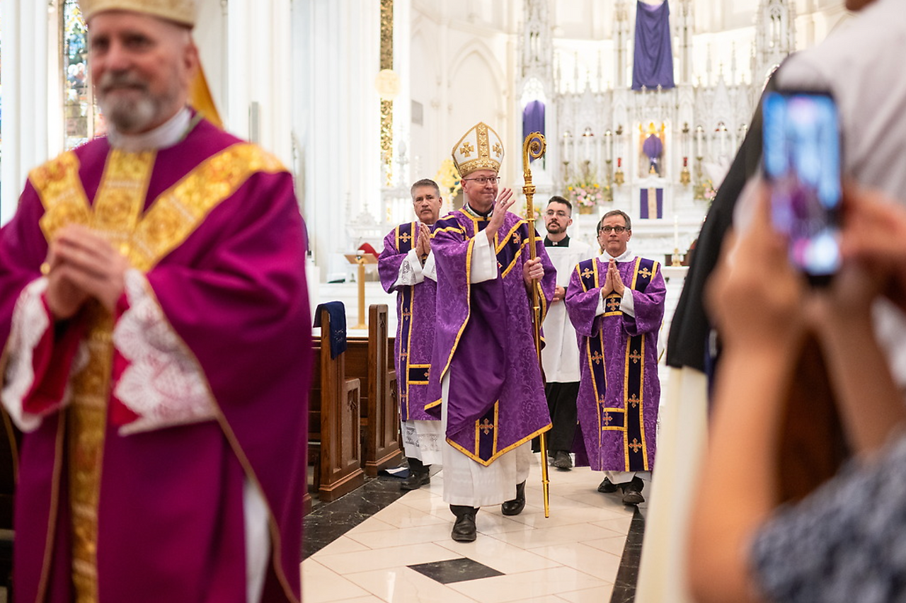 Obispo y sacerdotes en vestiduras moradas caminan en procesión por el pasillo central de la iglesia.