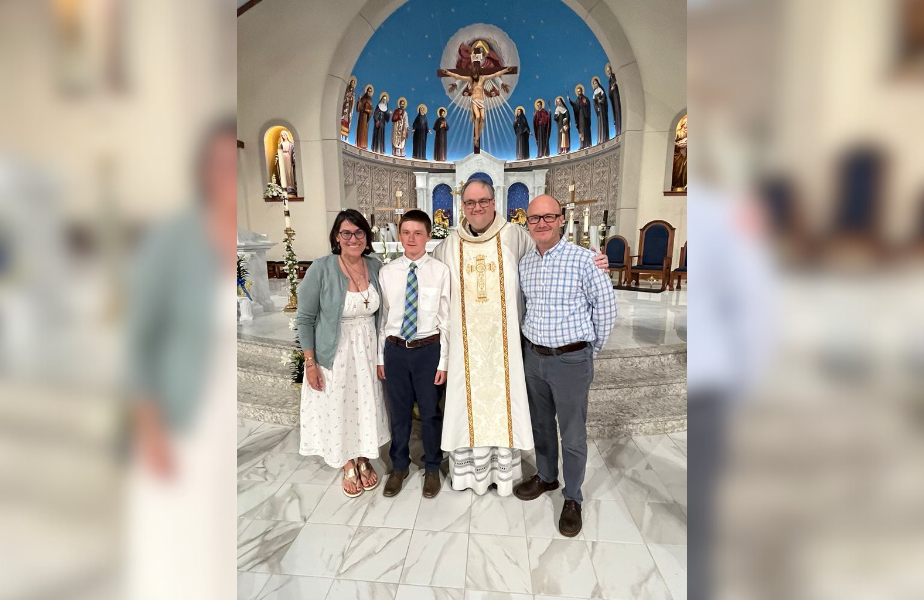 A family of four poses with a priest inside a church adorned with icons and a blue dome. The mood is joyful and celebratory.