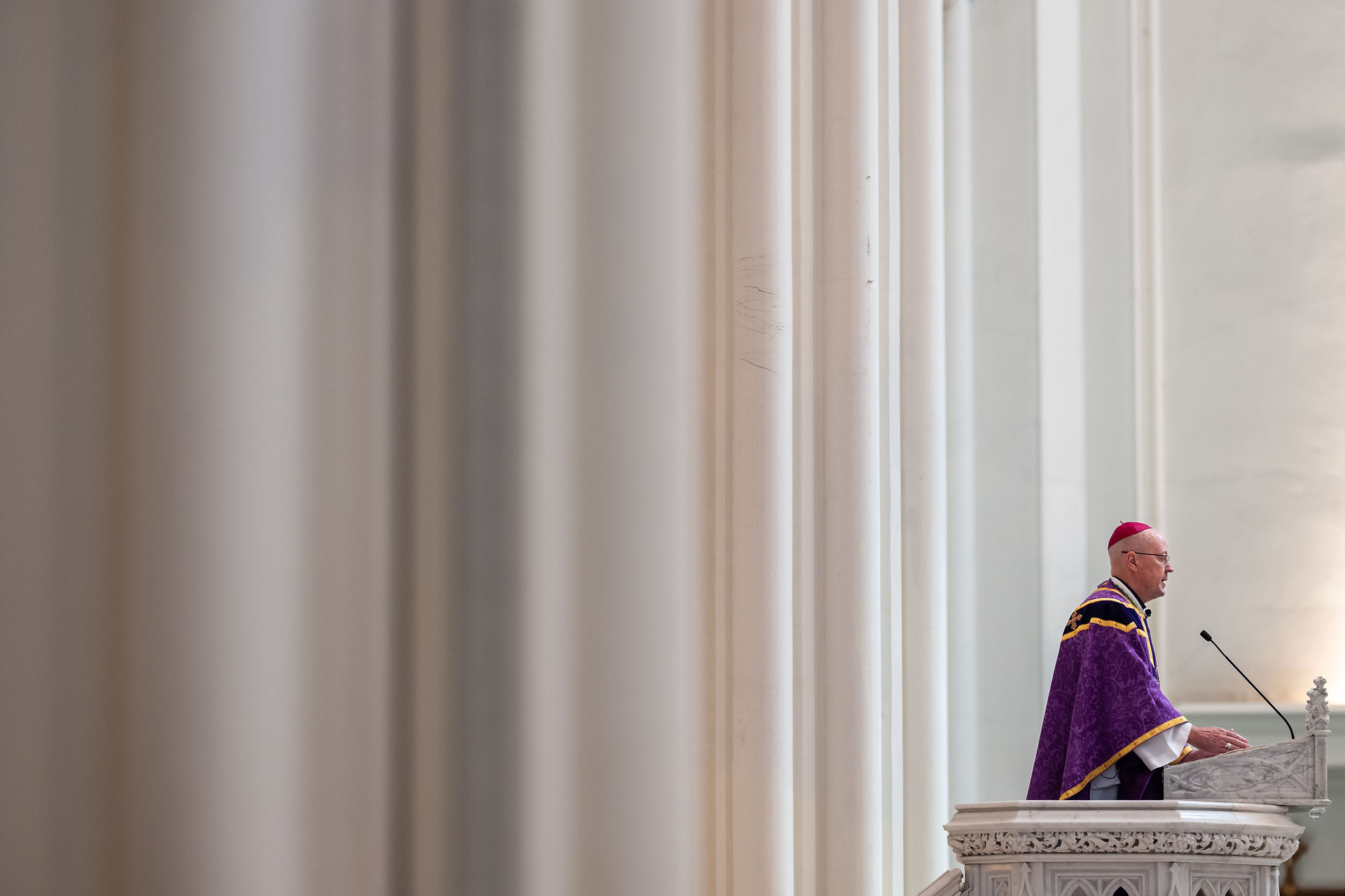 Obispo predica desde el ambón en una catedral amplia con columnas altas.