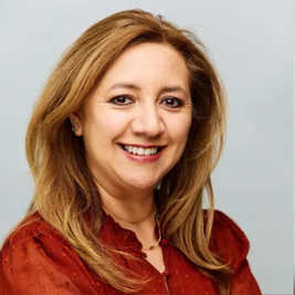 Smiling blonde woman in a red blouse posed against a light gray background, in a warm studio portrait.