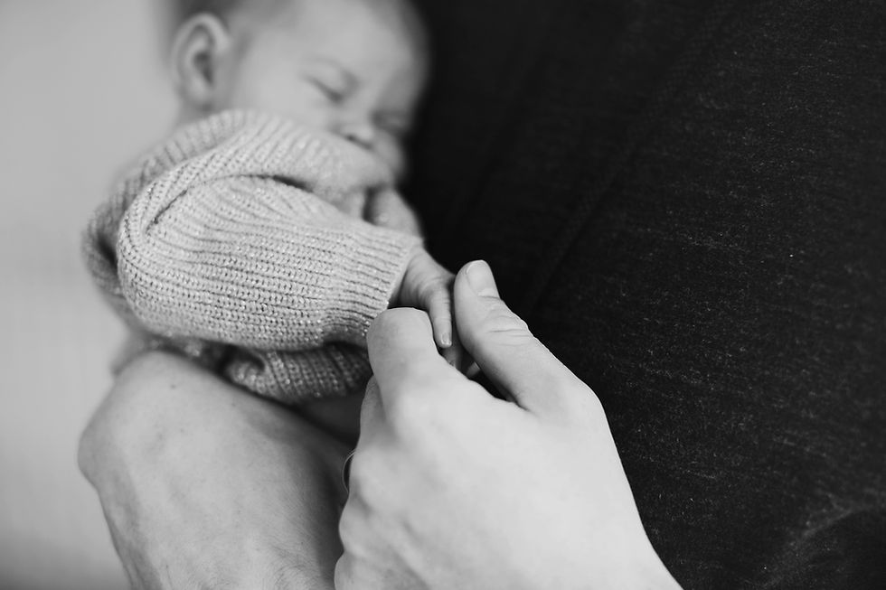 Black and white image of a baby sleeping in a knitted sweater, holding an adult's hand, evoking a tender and peaceful mood.