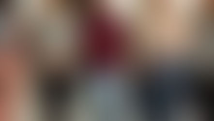 Five women stand arm-in-arm, smiling. They wear casual clothes in neutral tones. The background is plain, conveying a cheerful mood.