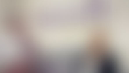 Woman smiling next to a cardboard cutout of a man. Background shows "FRASSATI Catholic Academy" text, with mountain imagery. Calm mood.