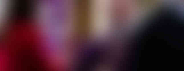 Bishop in purple robe gives Communion to a woman in a red jacket. Candles lit, purple banner with text in the background.