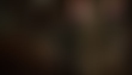 Two men stand in a dimly lit church with stained glass windows. One in a suit holds a hat, looking serious. Wooden pews line the aisle.