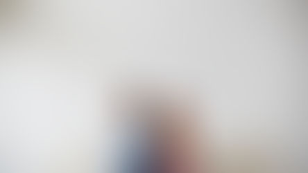 Two people sit back-to-back on a beige sofa, arms crossed, against a white brick wall. They appear upset or distant.