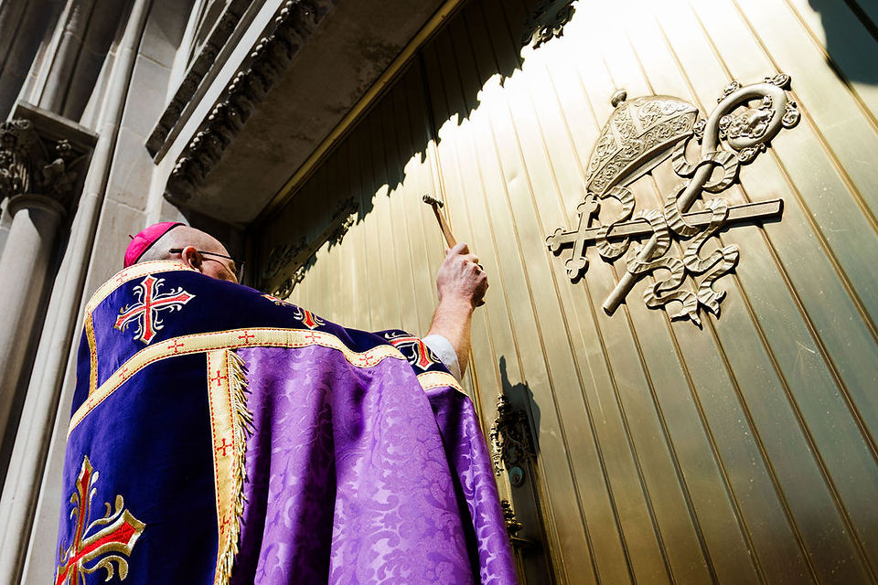 Obispo golpea una gran puerta de la iglesia con un pequeño martillo en un rito ceremonial.