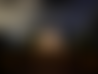 Illuminated path leading to a lit chapel at night, with glowing lanterns and cloudy sky. Trees frame the serene, inviting scene.