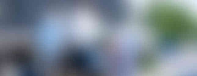 Four people walk along a sidewalk beside a parked truck with Braveheart branding. The setting is a sunny street with traffic signs.