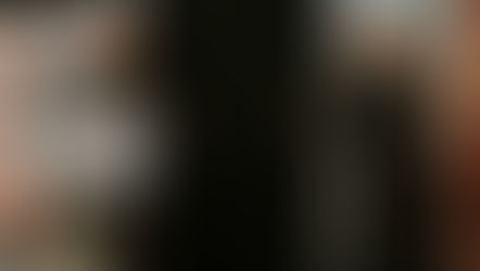 Two clergy members laughing on stage, one at a podium with a cross emblem. Background shows religious artwork, creating a joyful mood.