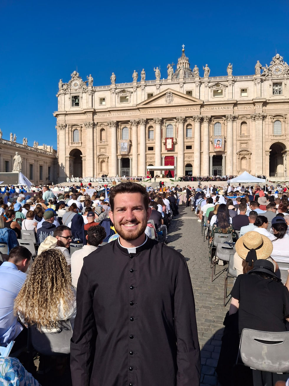 Smiling seminarian in black cassock stands before a crowd at St. Peter’s Square, with St. Peter’s Basilica under a blue sky.