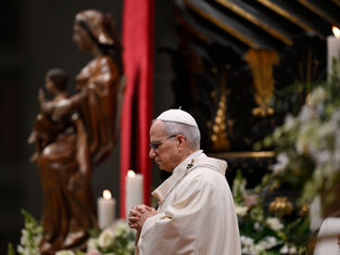 Cleric in white robe and cap prays with folded hands. Background shows a statue, red drape, and lit candles, creating a solemn ambiance.