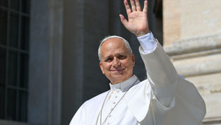 Pope in white robes smiles and waves from a balcony against a stone building backdrop, conveying a warm, welcoming mood