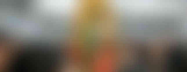 Statue of Virgin Mary with green and red robes and gold accents in a crowded church, surrounded by people in an observant mood.