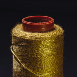 Close-up of a spool of golden thread with a deep red top against a dark background, highlighting the thread's sheen and texture.