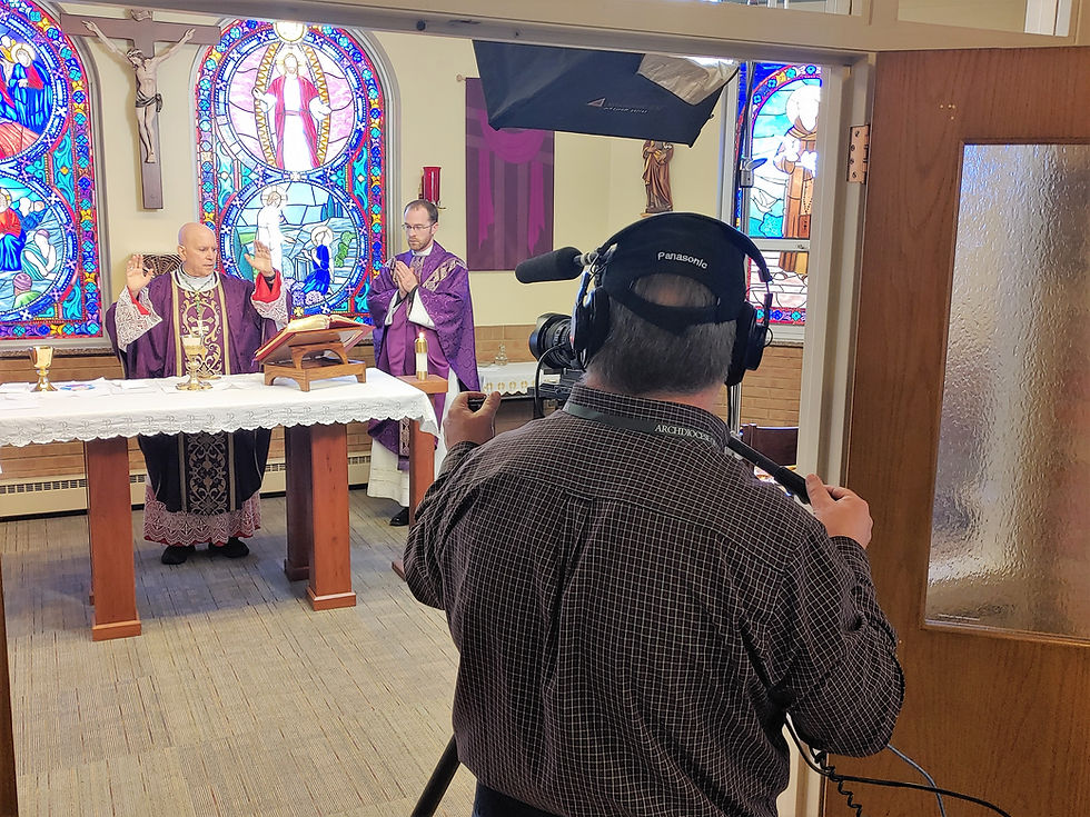 Clergymen in purple vestments conduct a service at an altar, framed by stained glass windows. A cameraman films from the side.