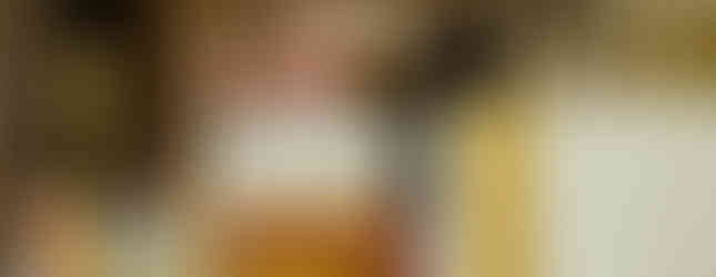 Priest raises a host during a Catholic Mass in a church. Candles and gold chalice on altar. Background features ornate architecture. Solemn mood.