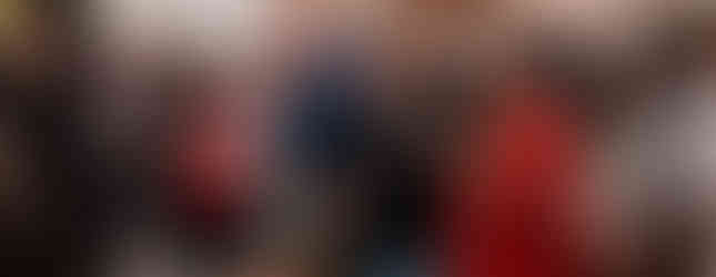 People in a church stand and read hymn books. The woman in red looks focused. Wooden pews and soft lighting create a solemn atmosphere.
