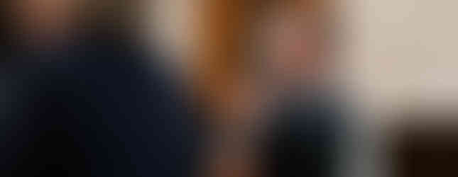 Man with a beard praying in a church, clasped hands, wearing a dark t-shirt. Wooden door in the background, peaceful atmosphere.