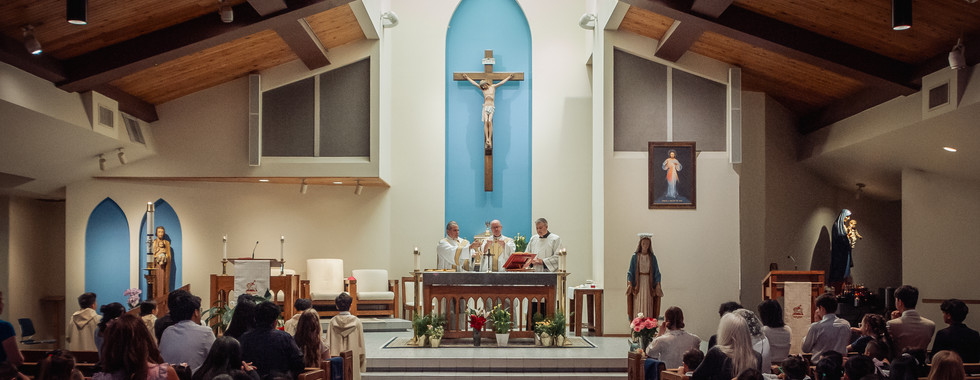 Congregation gathers for Catholic Mass inside a church sanctuary during the Eucharistic prayer and consecration.