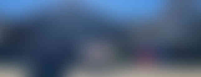 Dancers in vibrant dresses perform outside Saint Anthony church. Bright sun overhead, audience seated, colorful decorations and banners.