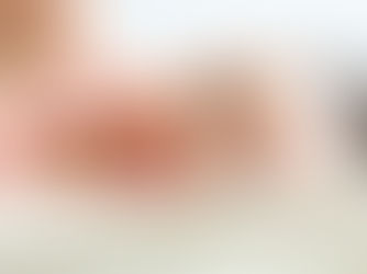 A smiling baby lies on a soft surface, wearing a pink shirt. The background is a light blur, adding a serene and joyful mood.